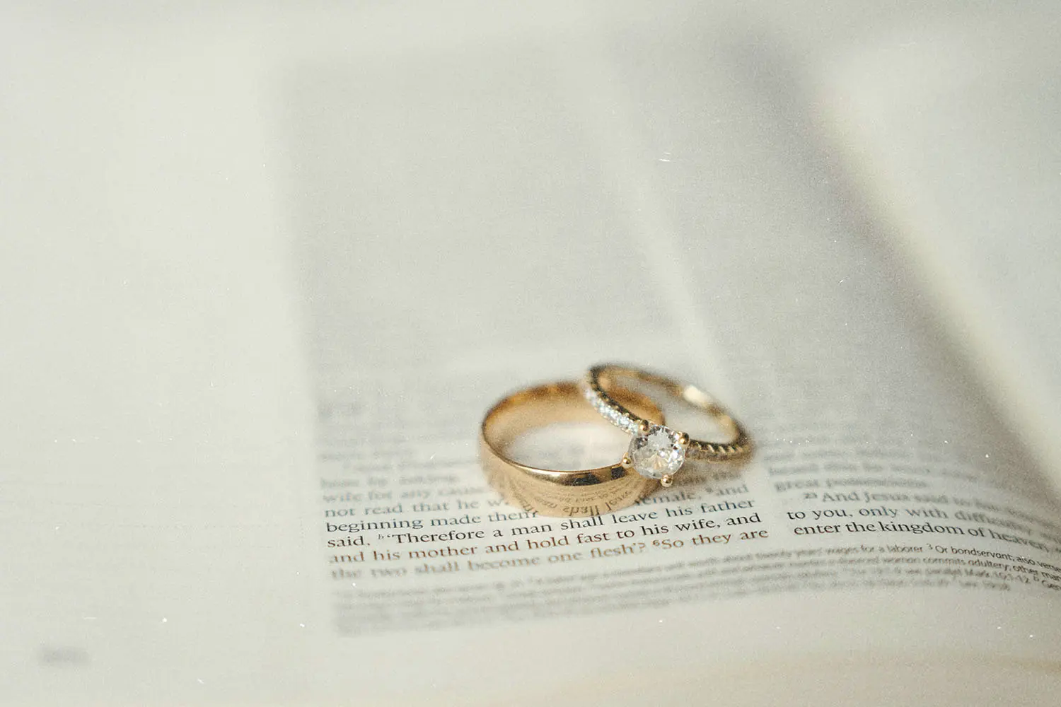 Gold wedding rings resting on an open Bible with the text softly blurred around them