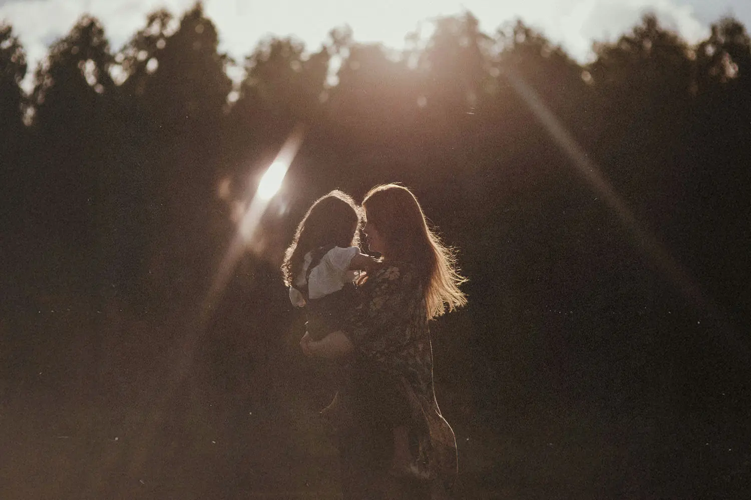 Silhouetted adult holding a small child in a sunlit clearing with trees in the background