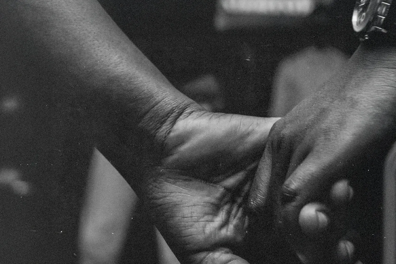 Close-up of two hands gently holding each other in a dark, softly lit setting