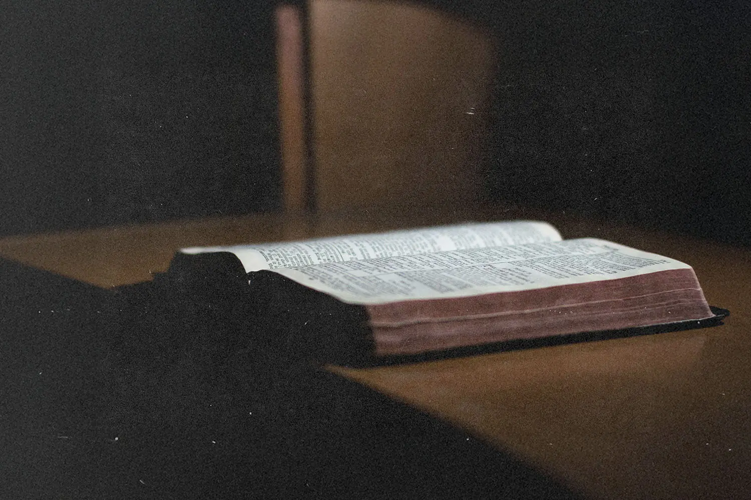 Open Bible resting on a wooden surface with soft light highlighting the printed text