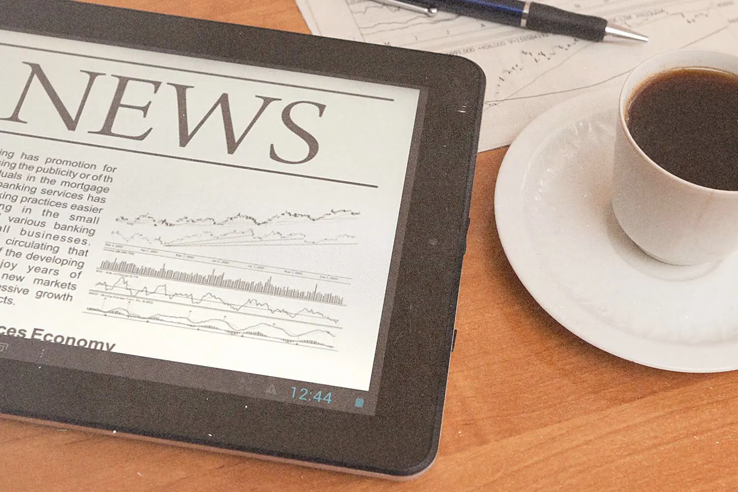 Tablet displaying a news webpage beside financial papers, a pen, and a cup of coffee on a wooden table