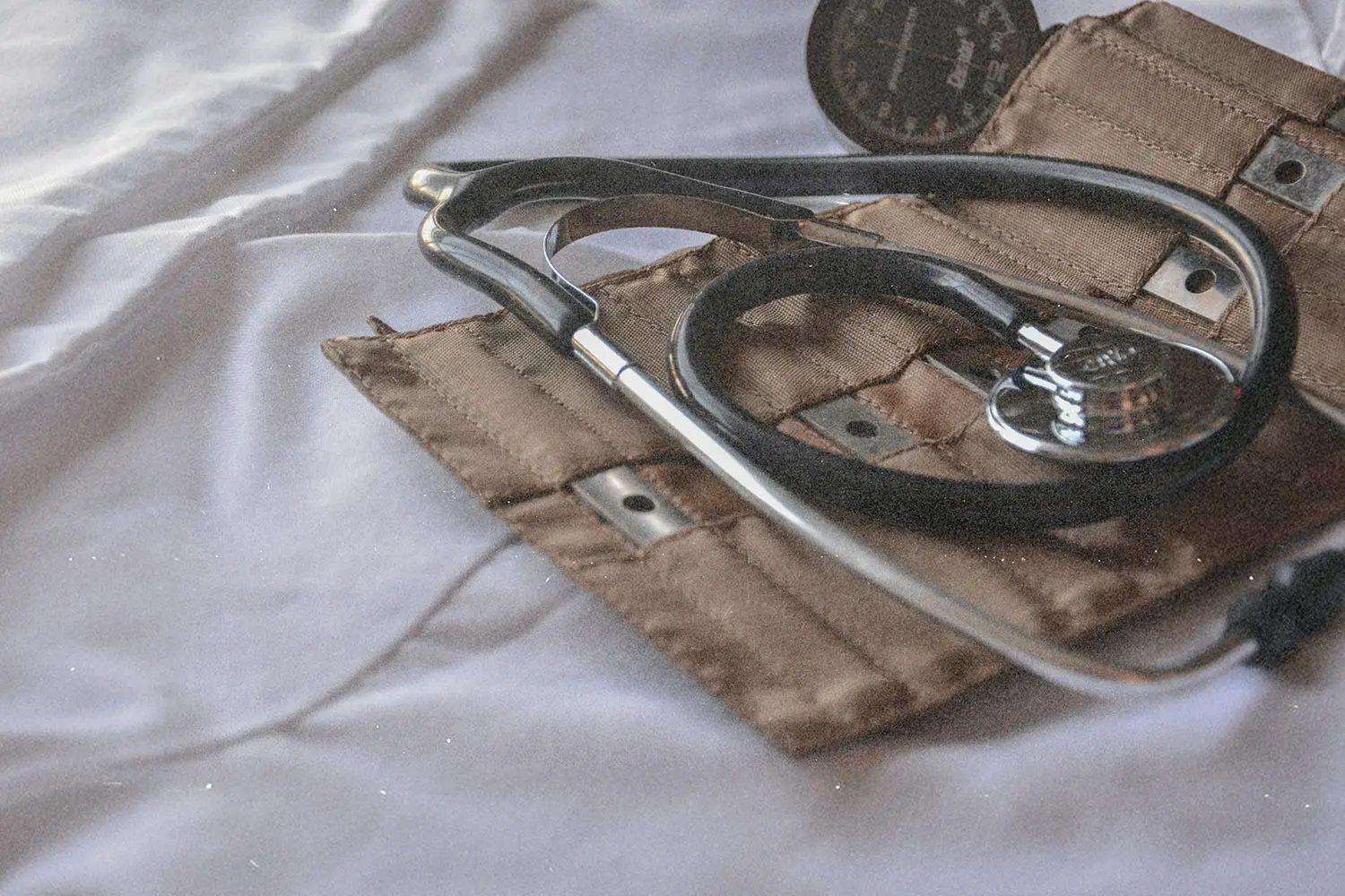 Stethoscope resting on a folded blood pressure cuff atop a white fabric surface