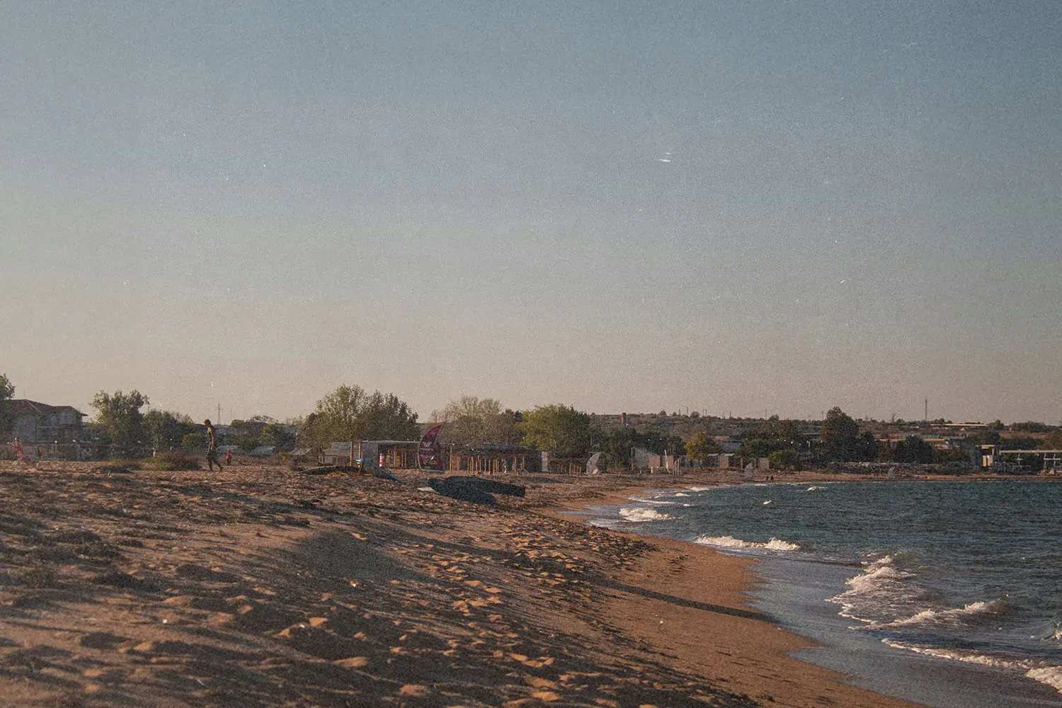 Quiet sandy beach with gentle waves and a distant shoreline lined with trees and small buildings