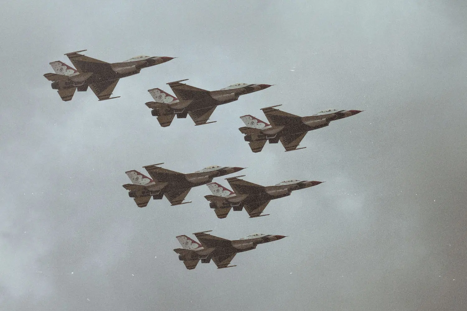 Formation of six military fighter jets flying together through a cloudy sky