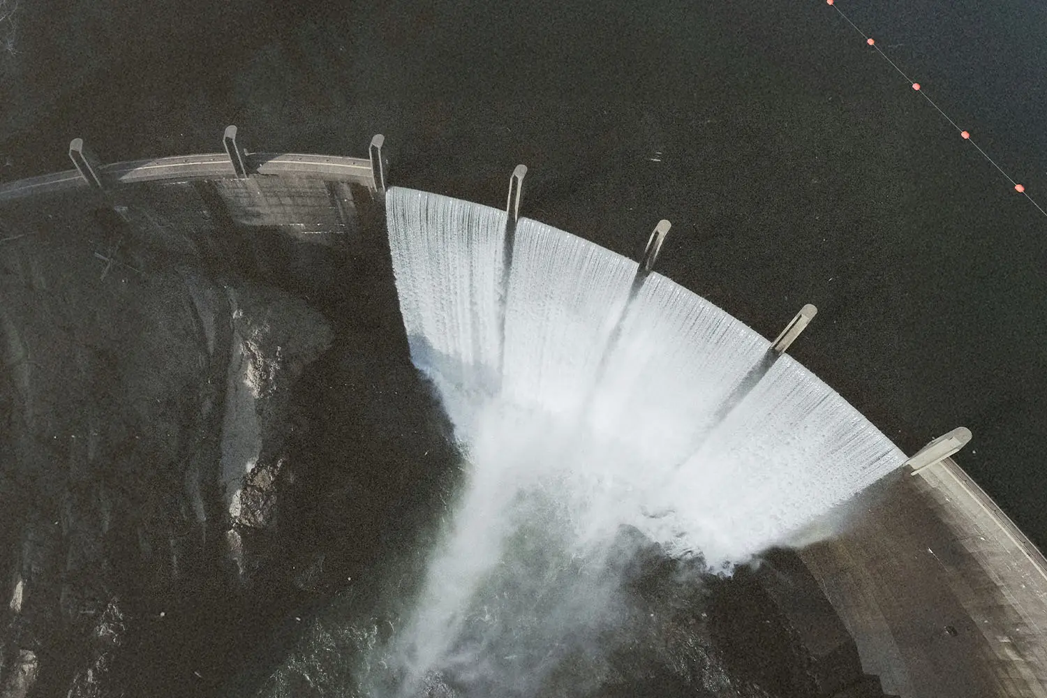 Aerial view of water cascading over the curved spillway of a large dam into the basin below