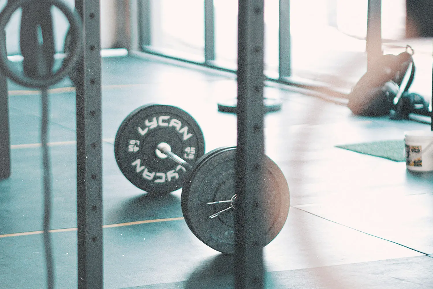 Loaded barbell resting on the floor of a gym near squat racks and natural window light