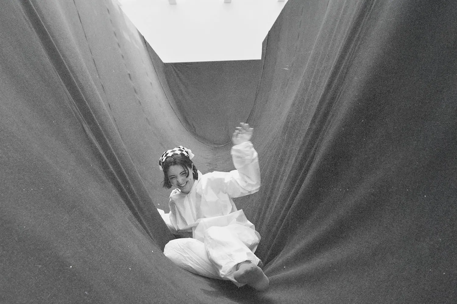 Person sliding down a large fabric tunnel structure inside a bright indoor space