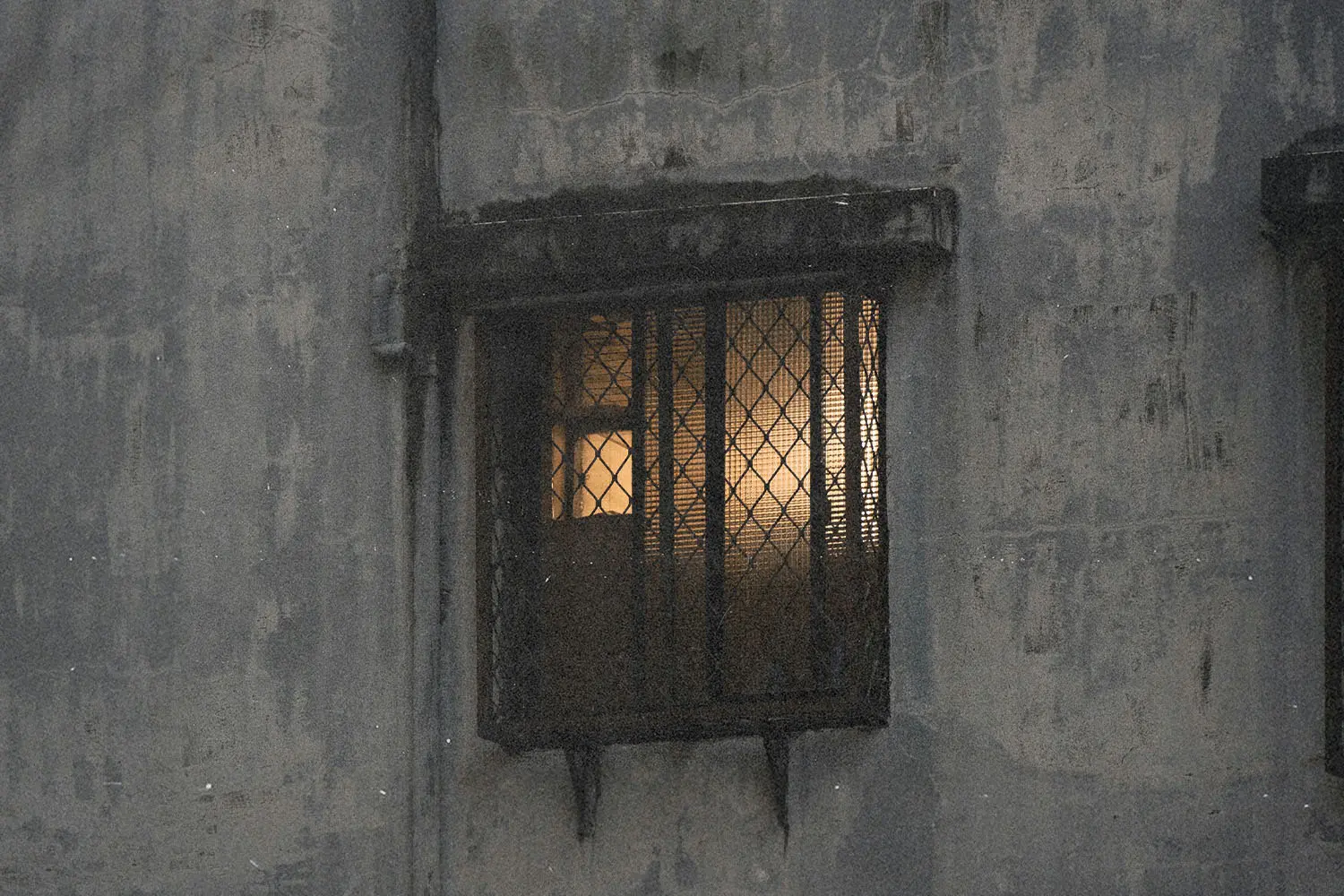 Warm light shining through a barred window on a weathered exterior wall