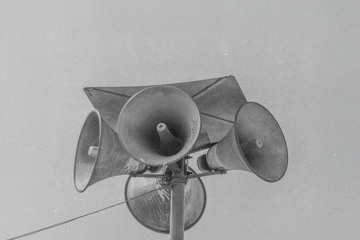 Cluster of large outdoor loudspeakers mounted on a tall metal pole against the sky