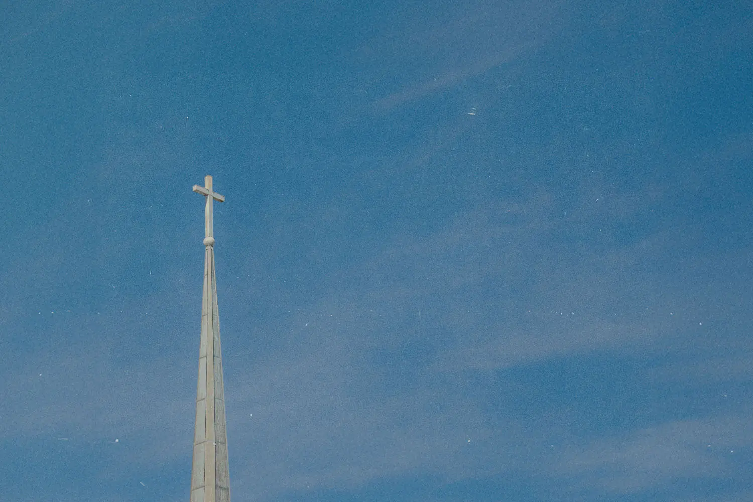 A church steeple with a cross at the top rises into a clear blue sky