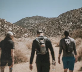 Three hikers walking along a dusty trail toward rugged mountain terrain