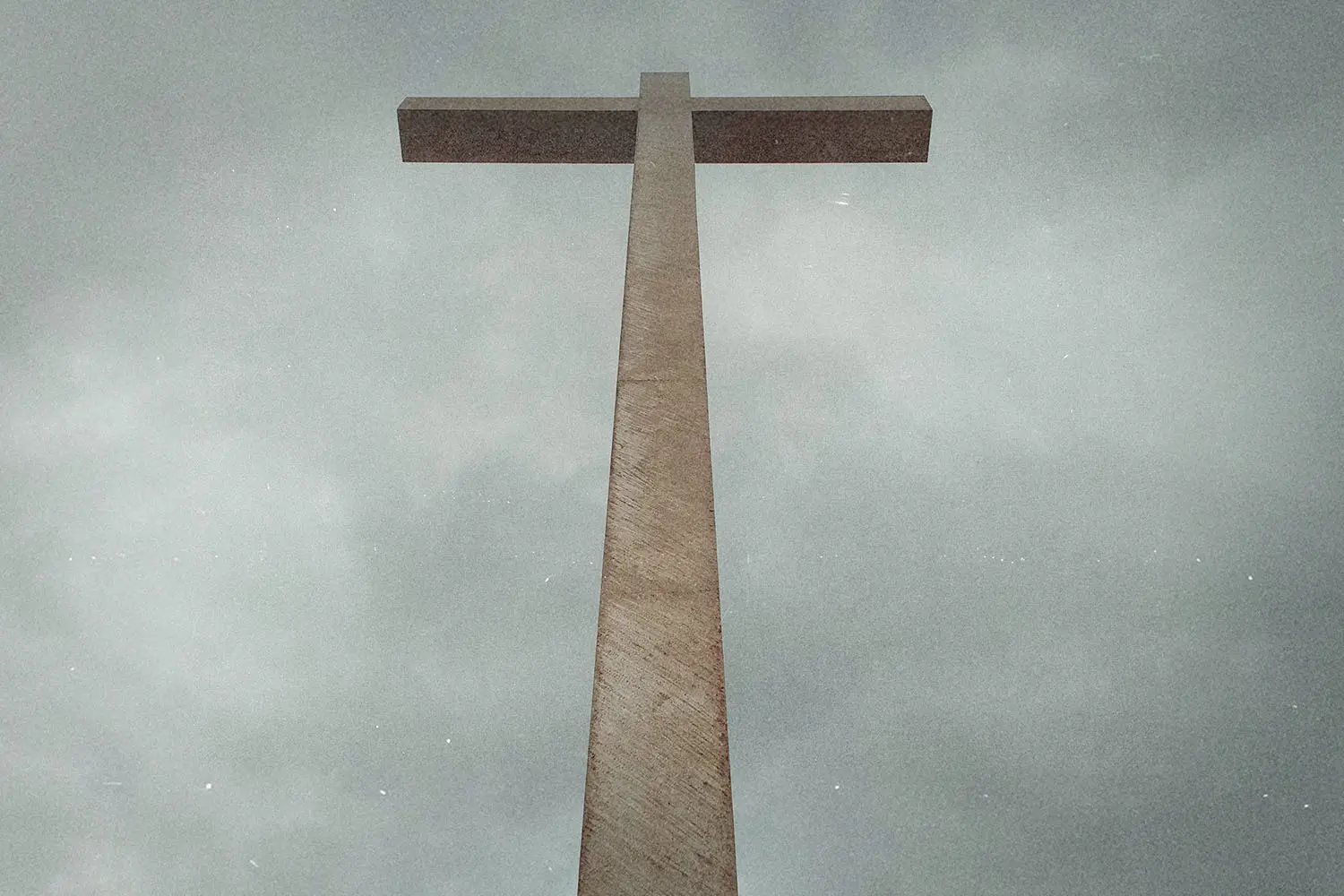 Tall cross-shaped structure photographed from below against a cloudy gray sky