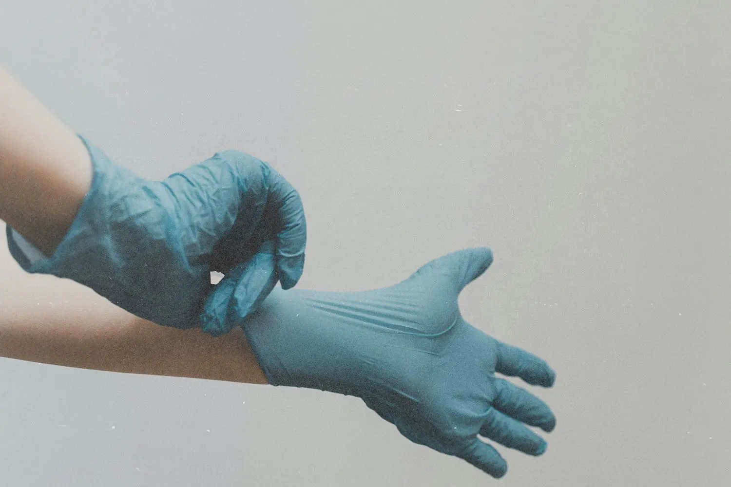 Hands pulling on a pair of blue disposable medical gloves against a plain background