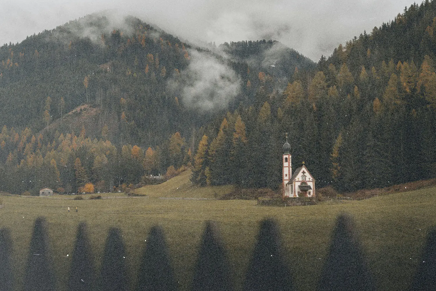 Small countryside chapel set in a misty mountain valley surrounded by dense autumn trees.