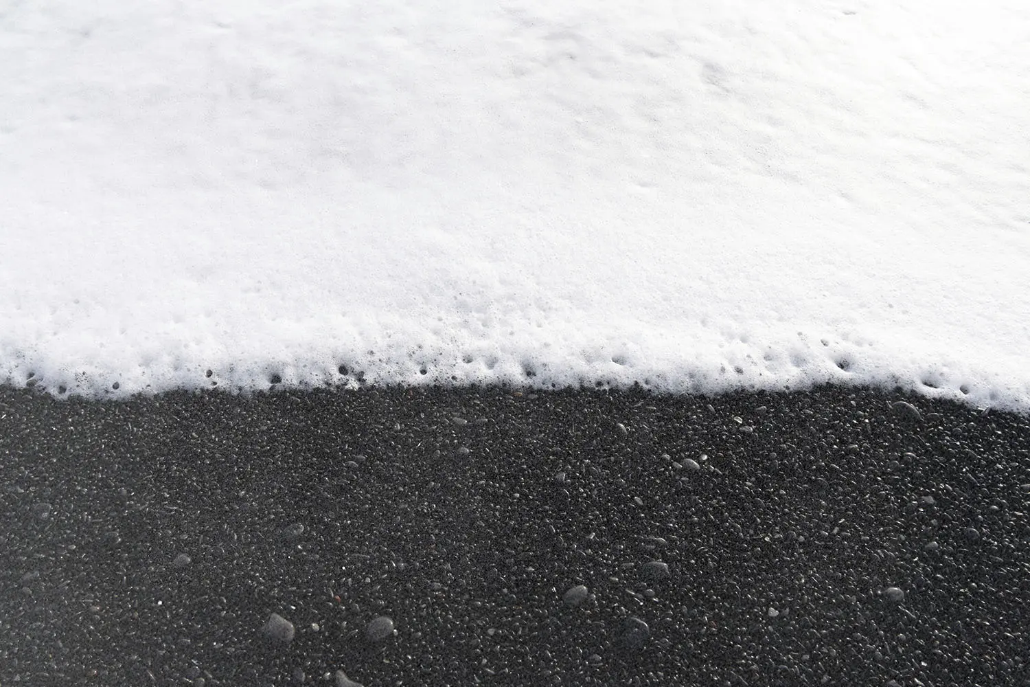 Ocean foam washing over dark pebbled sand as a gentle wave reaches the shoreline