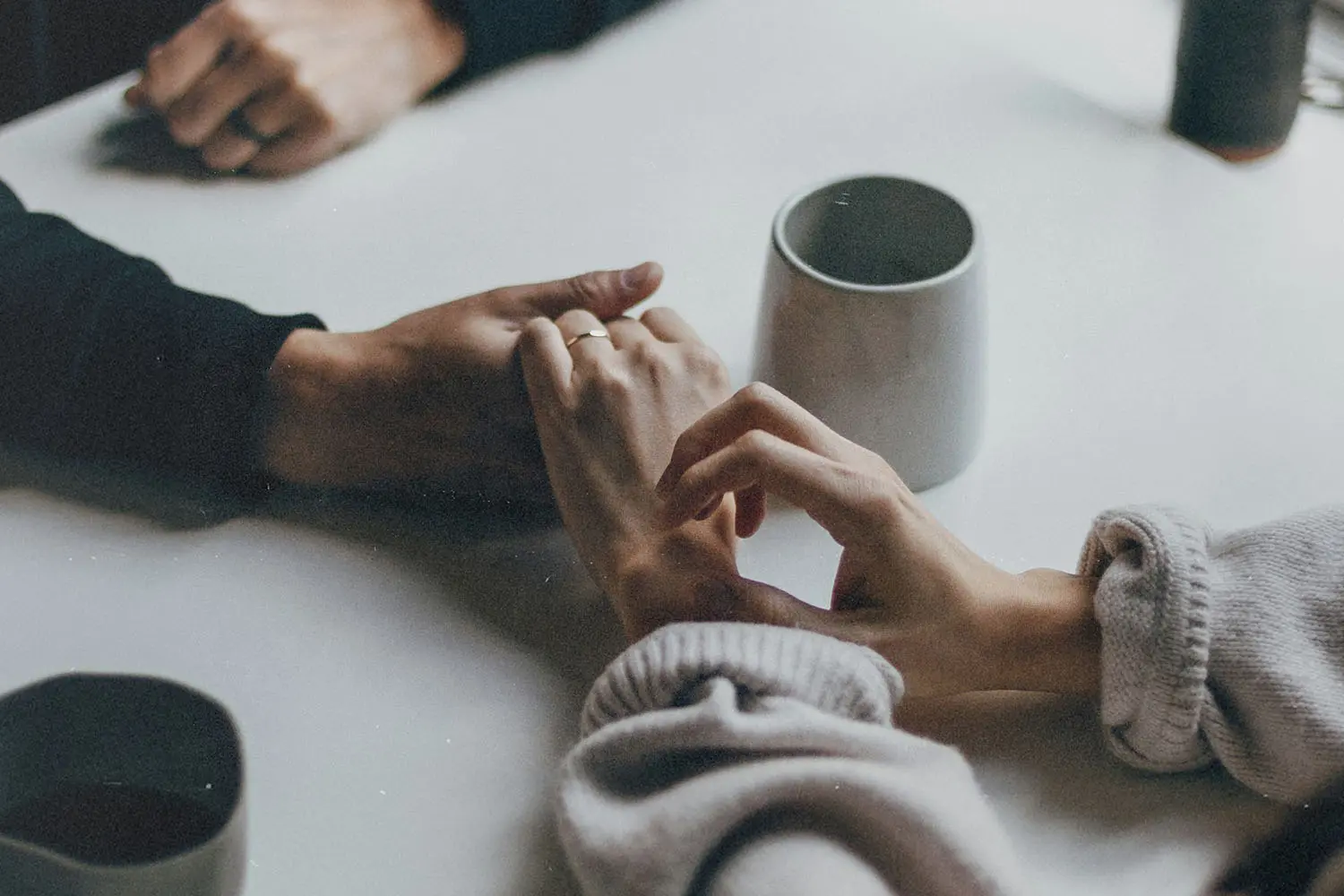 Two people sitting at a table holding hands beside ceramic coffee mugs