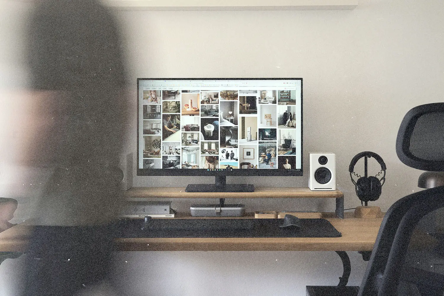 Home workspace featuring a computer monitor displaying a grid of images, with a desk, chair, and headphones on a stand
