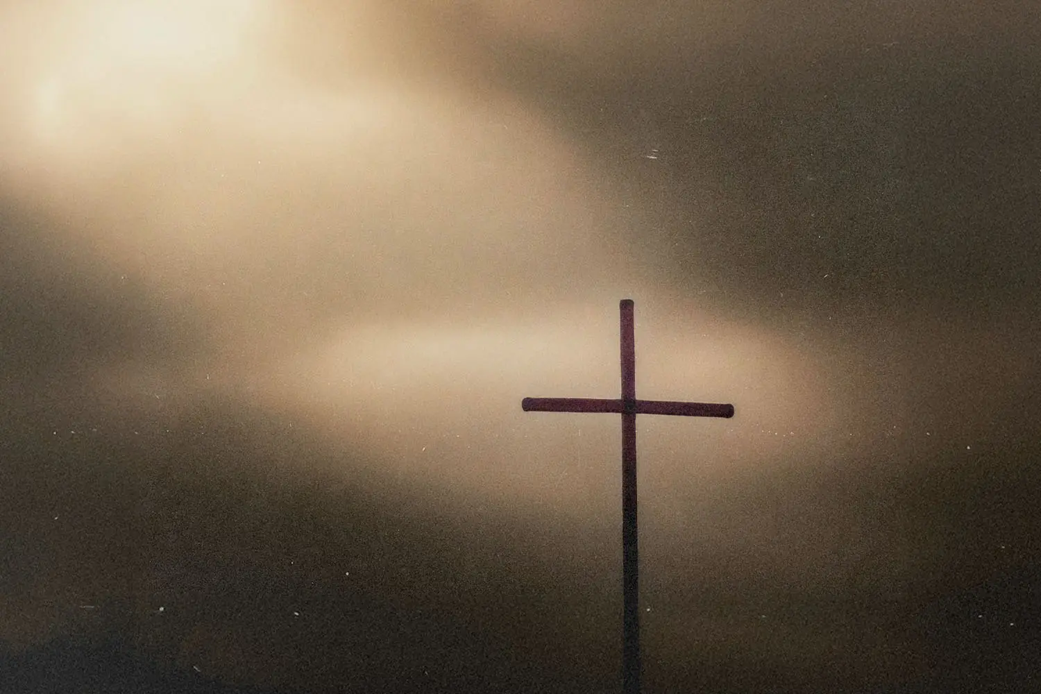 Simple wooden cross silhouetted against a sky with glowing, diffused light