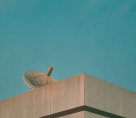 Satellite dish mounted on the corner of a concrete building against a clear blue sky