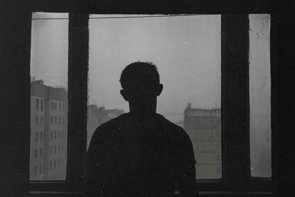 black and white photo of man standing in front of a window