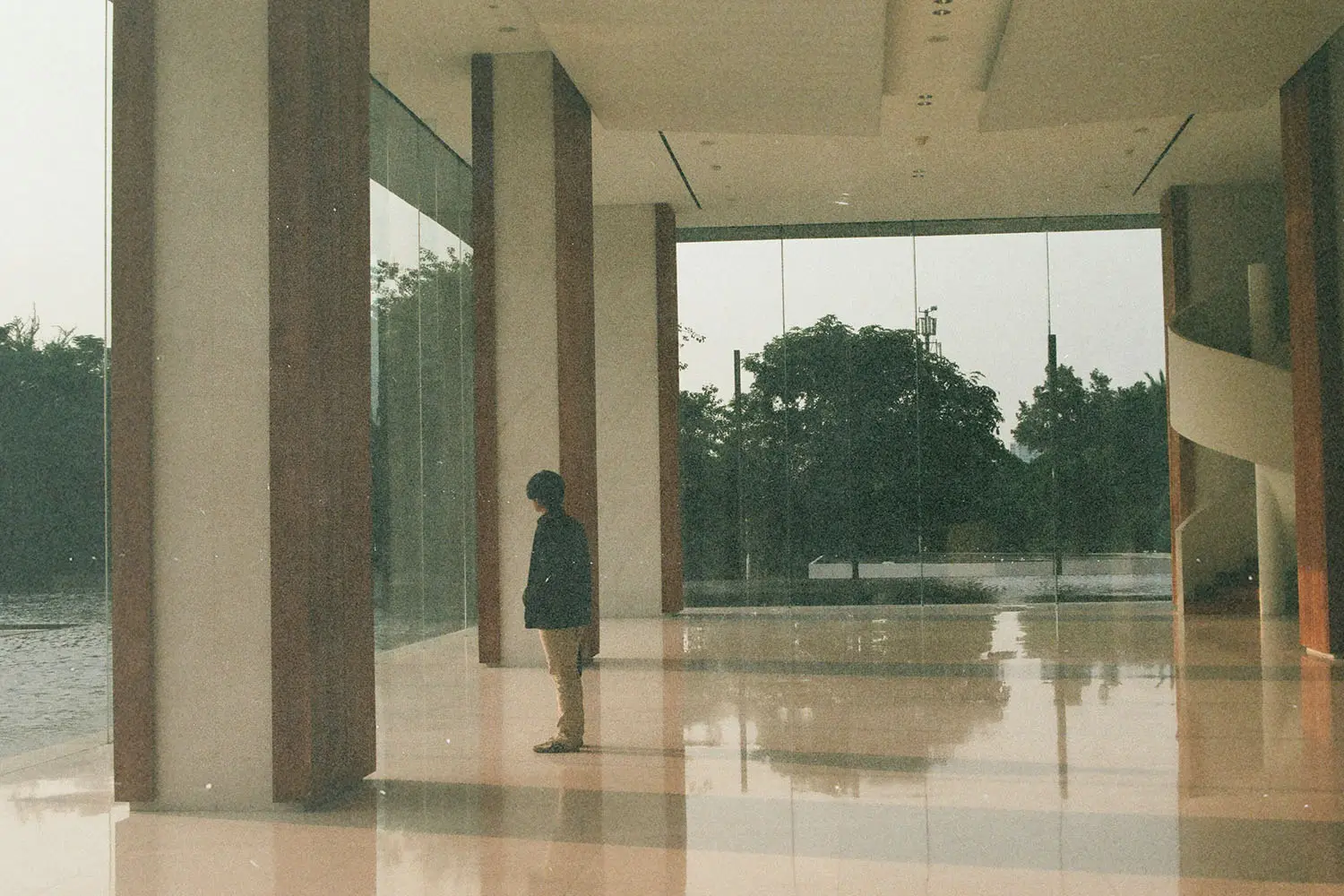 A person standing alone inside a modern building with glass walls.