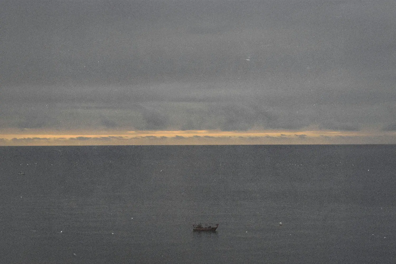 A small boat floating on calm water beneath a cloudy sky.
