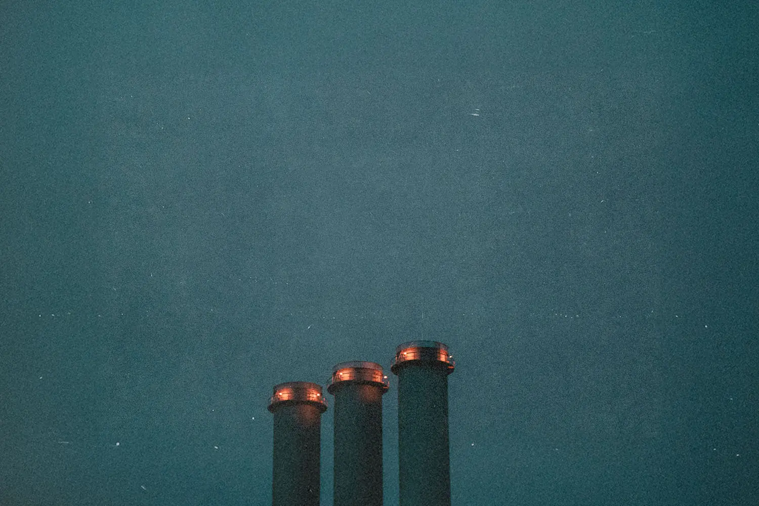 Industrial smokestacks rising against a dark sky.