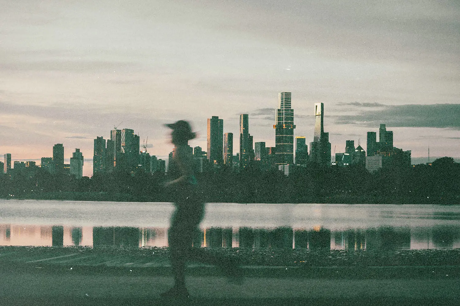Silhouetted runner moving along a lakeside path with a city skyline reflected in the water at dusk