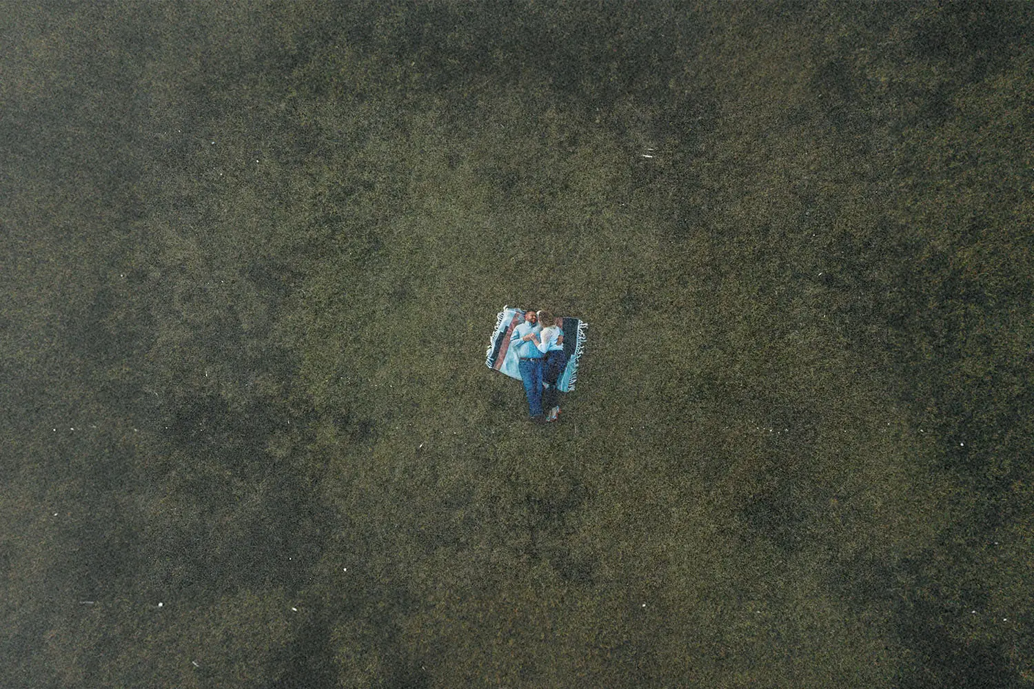 An aerial view of two people sitting closely together on open grassy land.
