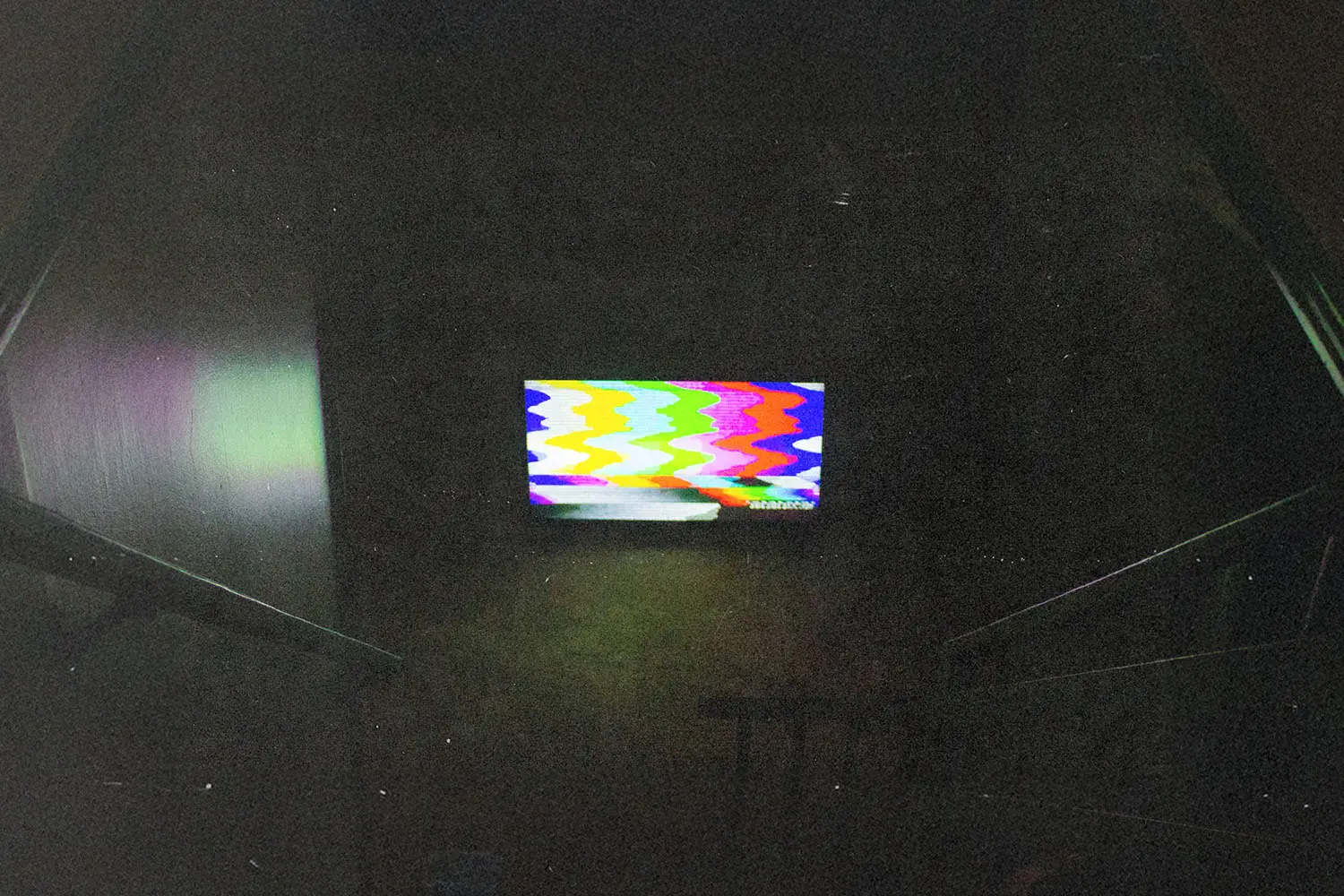 A dark room with a glowing television screen displaying distorted, colorful static.