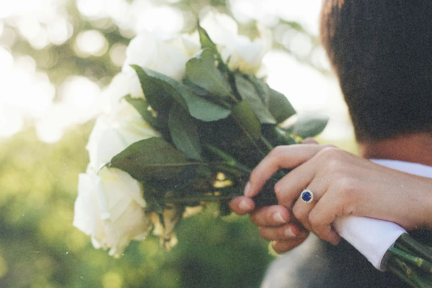 A close-up of hands holding a bouquet with wedding attire visible.