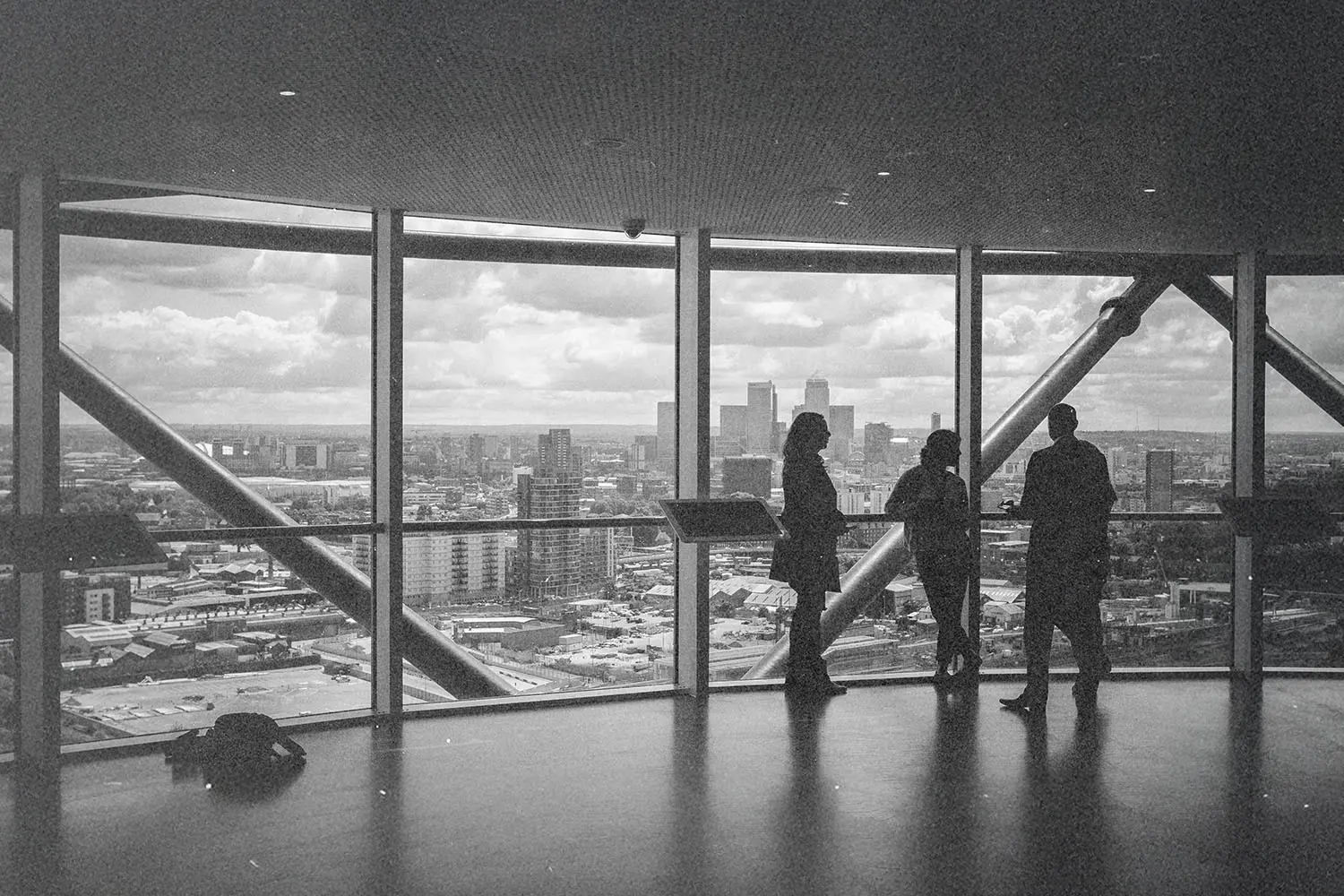 Three people standing near large windows overlooking a city.