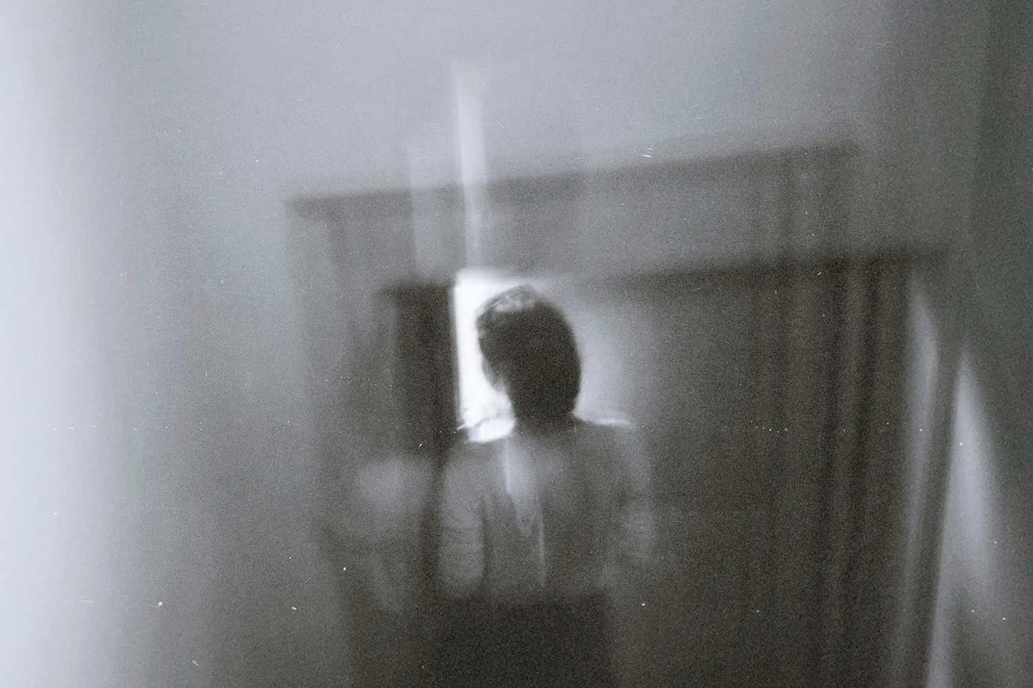 A blurred, reflective indoor image showing a solitary figure behind glass.