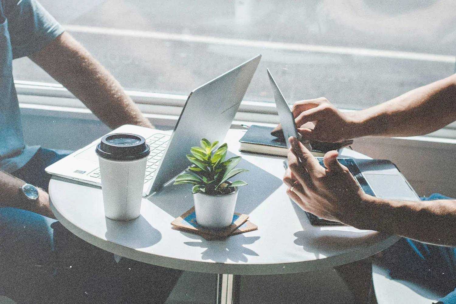 Two people working on laptops at a small round table.