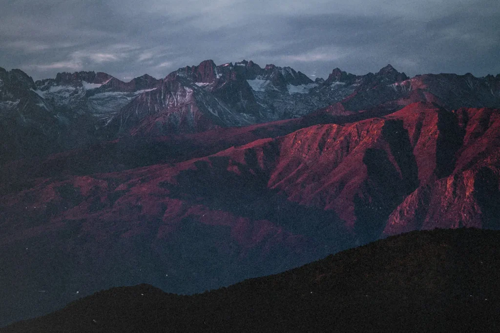 Mountain range at sunset with rugged peaks and slopes glowing red under dramatic clouds