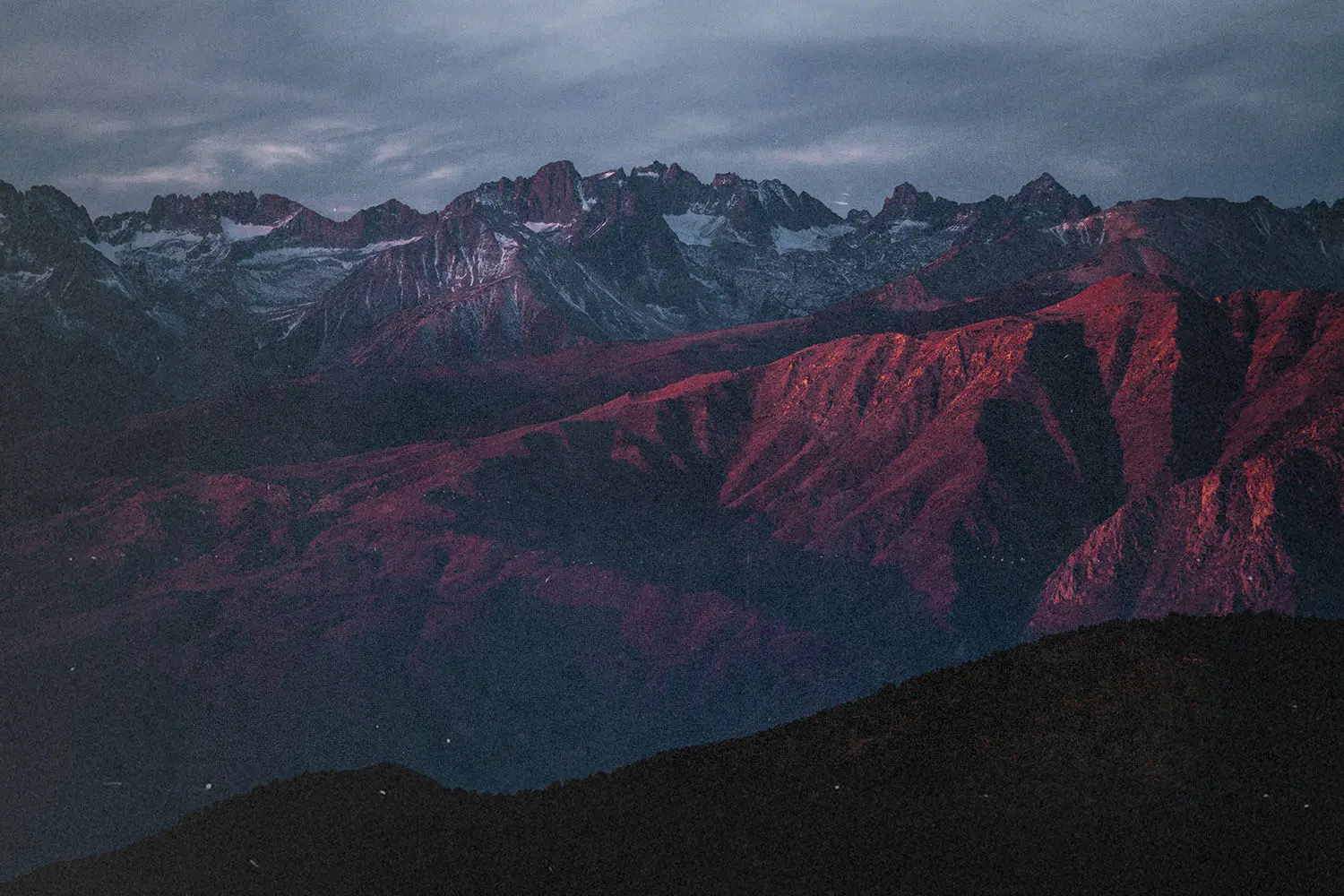 Mountain range at sunset with rugged peaks and slopes glowing red under dramatic clouds