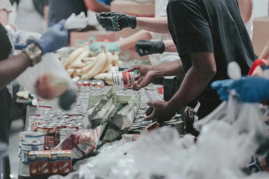 Volunteers sort and distribute canned goods, produce, and packaged food items along a long table at a community food‑drive event