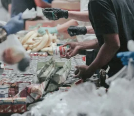 Volunteers sort and distribute canned goods, produce, and packaged food items along a long table at a community food‑drive event