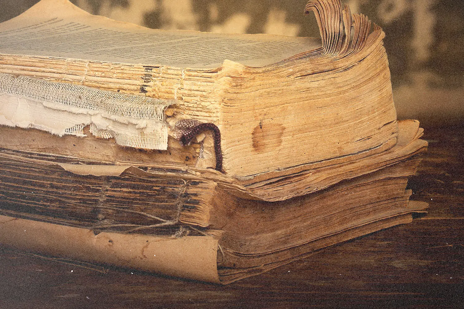 A close-up of old, worn books stacked on a wooden surface with frayed pages.