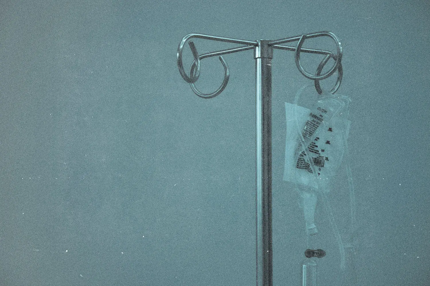 A medical IV stand with tubing and a fluid bag hanging against a plain background.
