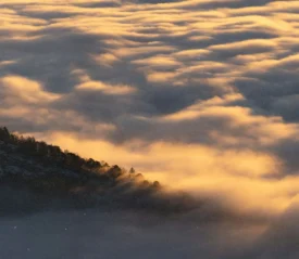 Golden clouds blanket a mountain landscape at sunrise or sunset, with warm light streaming across the ridges