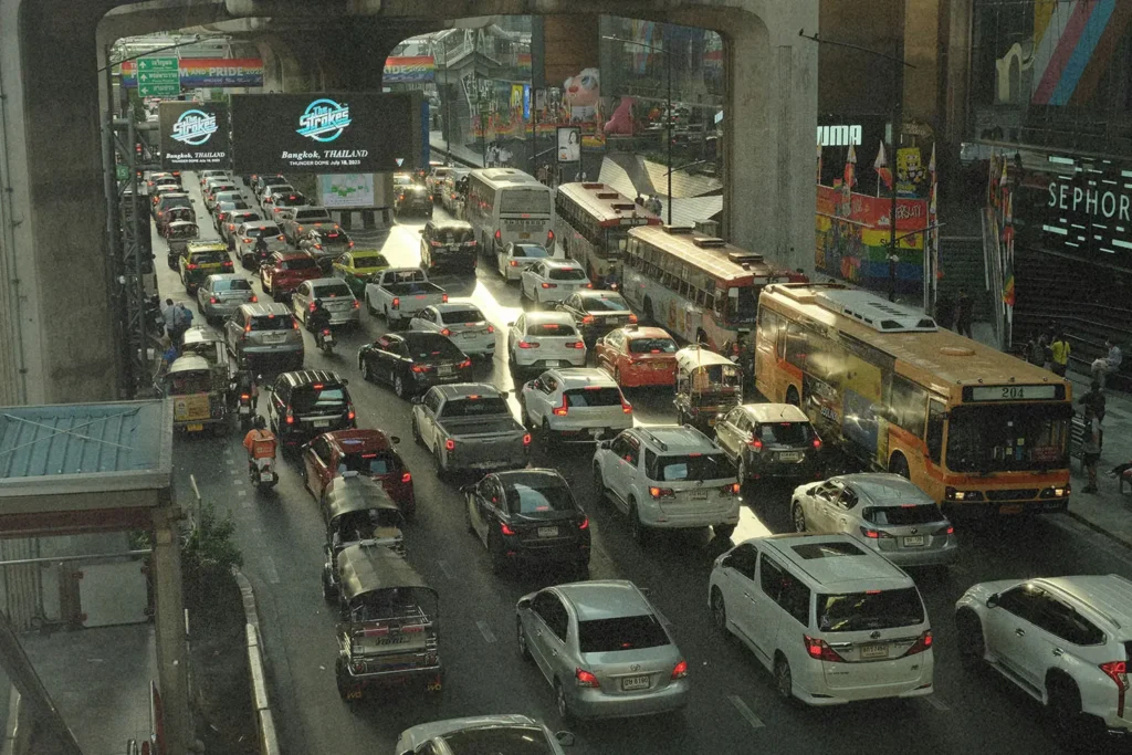 Heavy traffic jam on a multi‑lane city street filled with cars, buses, and tuk‑tuks beneath an elevated roadway in a busy urban shopping district