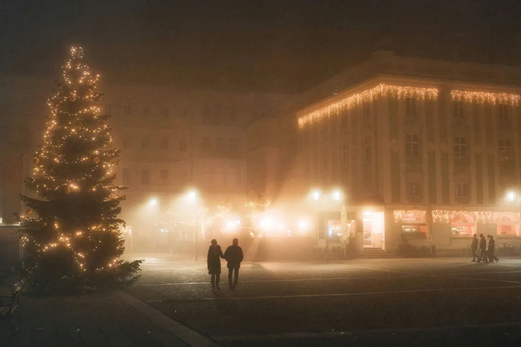 two people walking down lit street with snow all around and a lit christmas tree