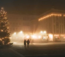 two people walking down lit street with snow all around and a lit christmas tree