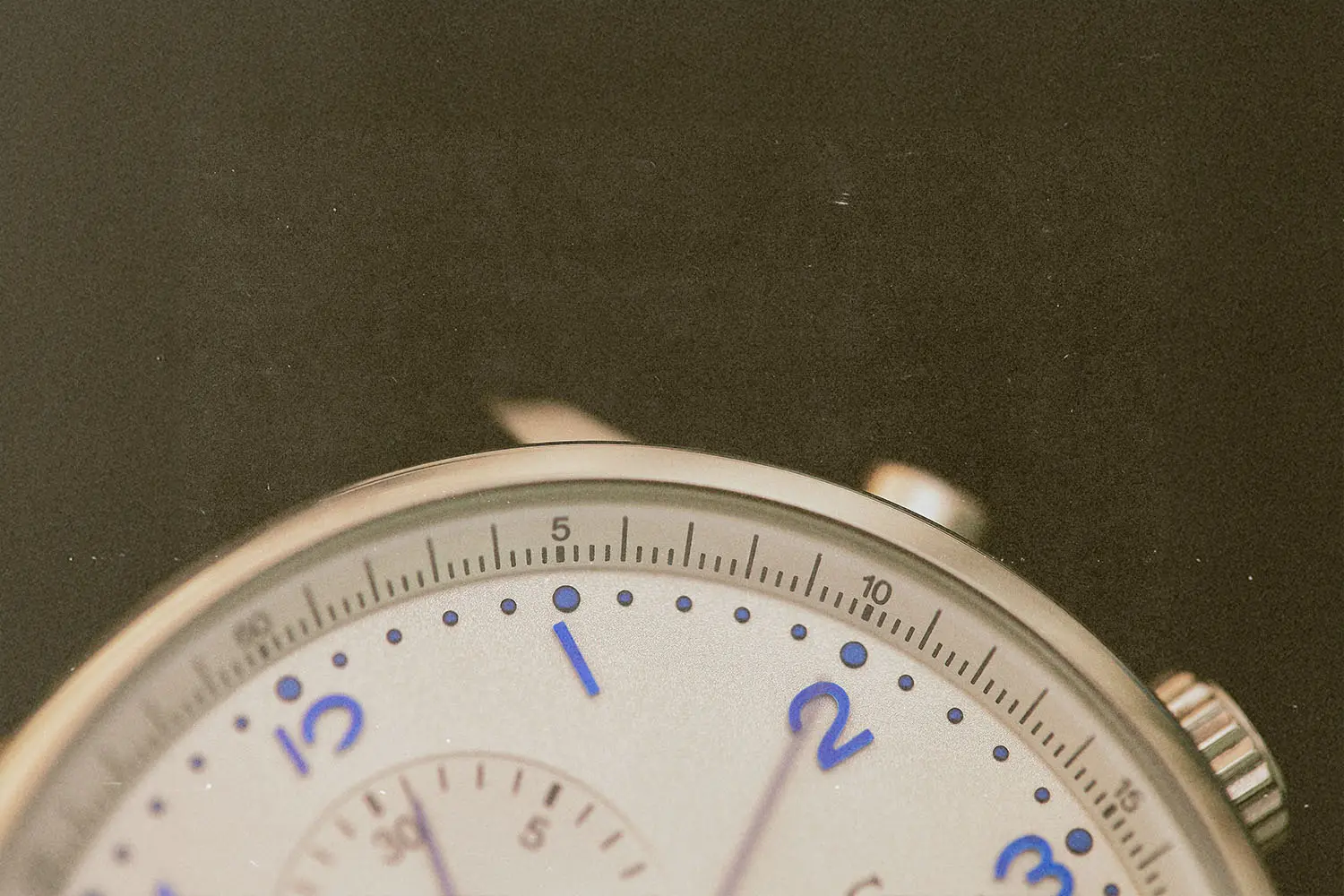 Close-up view of an analog watch face showing the numbers one through three and fine minute markings, with a metal casing partially visible against a dark background