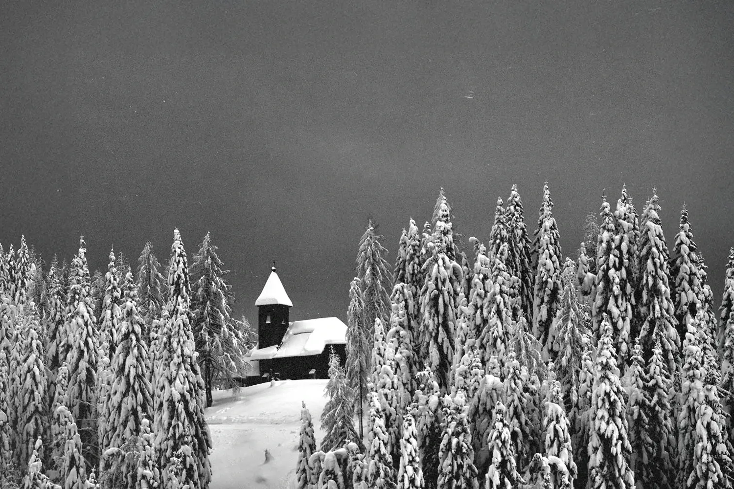 black and white photo of a church like building in the middle of a snowy forest