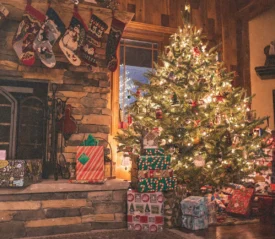Lit Christmas tree with presents underneath and stockings hung above the fire place