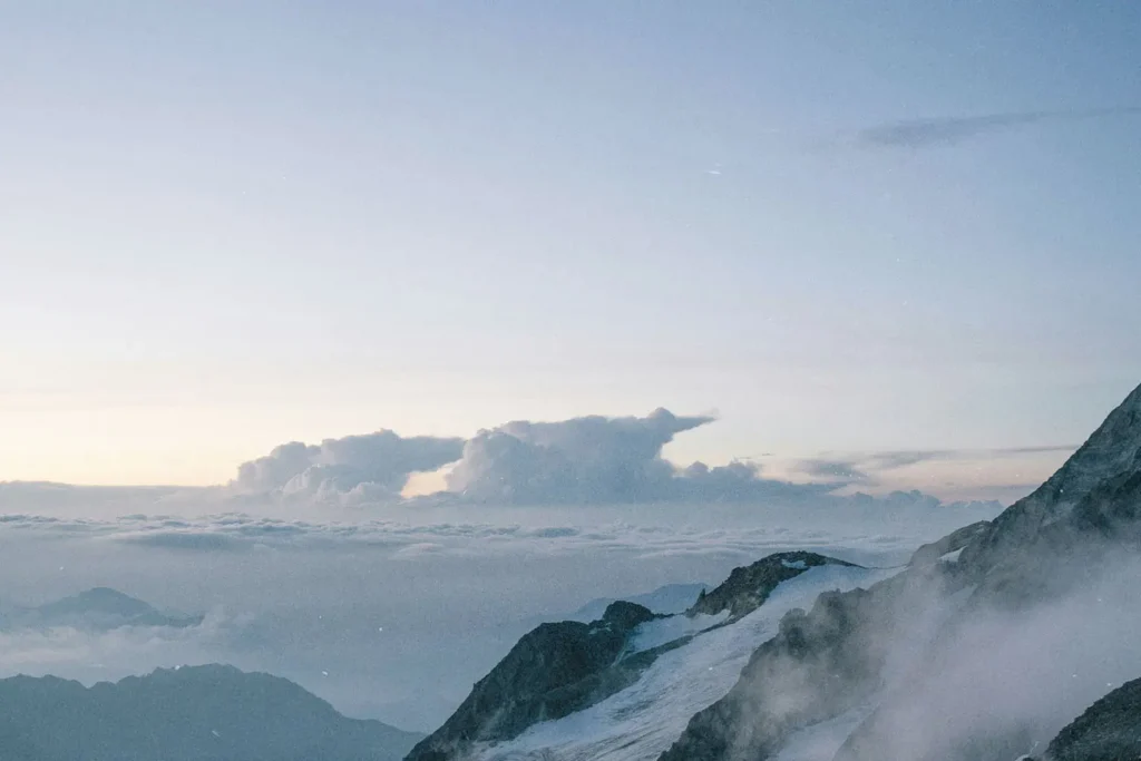 A serene mountain landscape with snowy peaks and clouds stretching across the horizon at sunrise or sunset