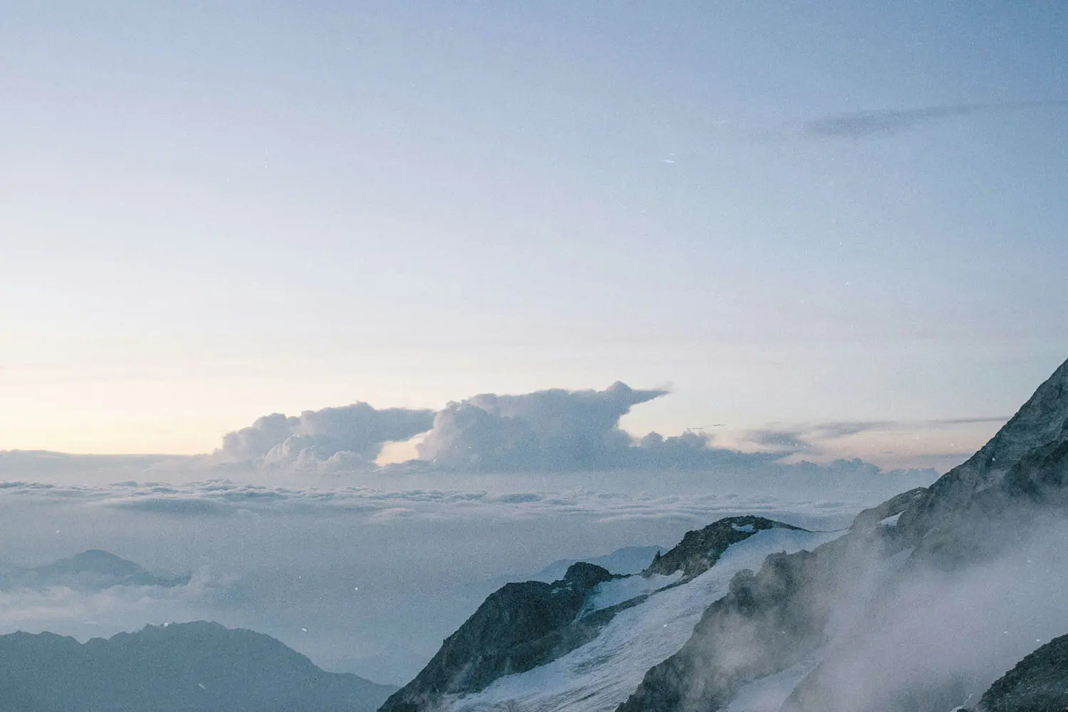 A serene mountain landscape with snowy peaks and clouds stretching across the horizon at sunrise or sunset