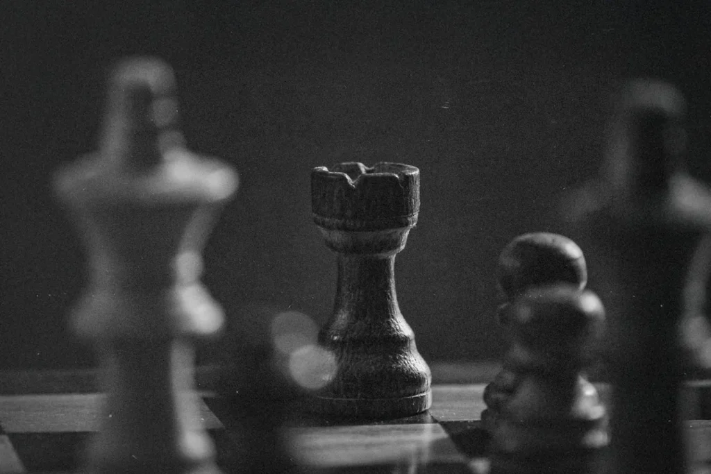 Black-and-white photograph of a chessboard with a wooden rook in sharp focus among blurred pieces